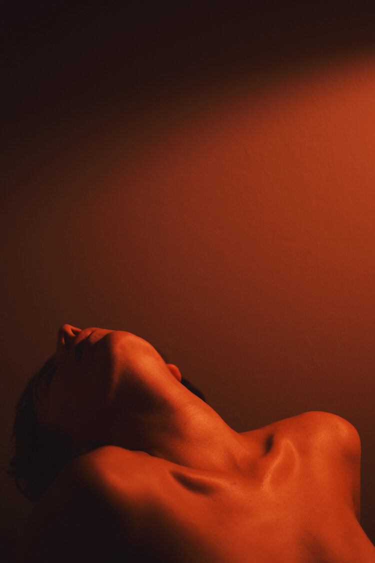 Naked person lying on a dark surface with warm lighting